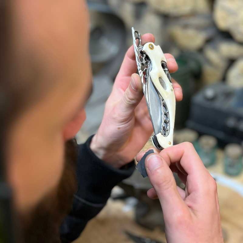 Ianis Fortin (Dracoforge) réalisant des finitions sur un couteau pliant Neptune à l'atelier